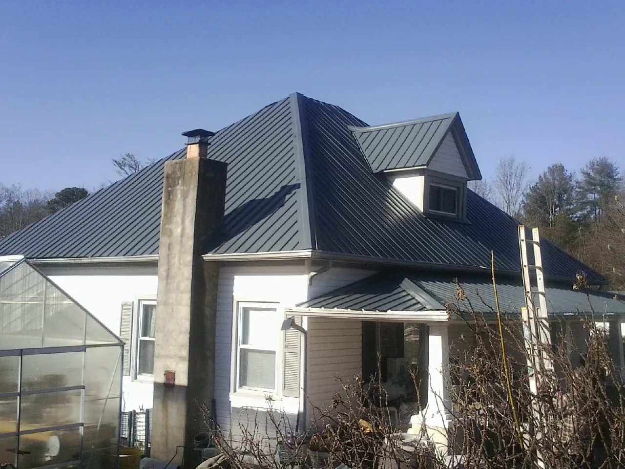 Dark blue standing seam metal roof on a white farmhouse with dormer — Slate & Tile Roof Repair by Roofing Brothers in Milnor