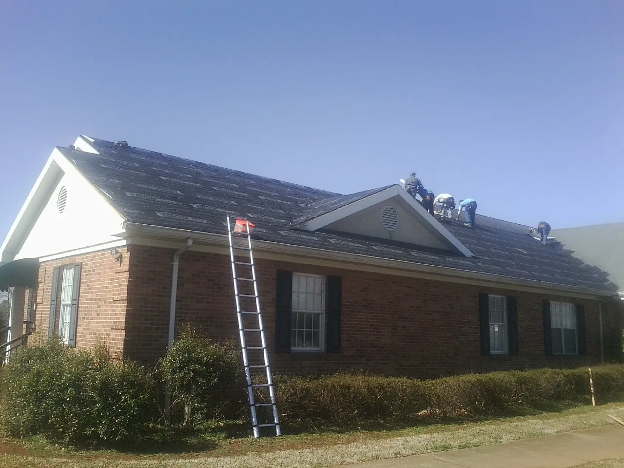 Crew tearing shingles off a brick ranch roof with a ladder set — Emergency Roof Repair work by our crew in Milnor