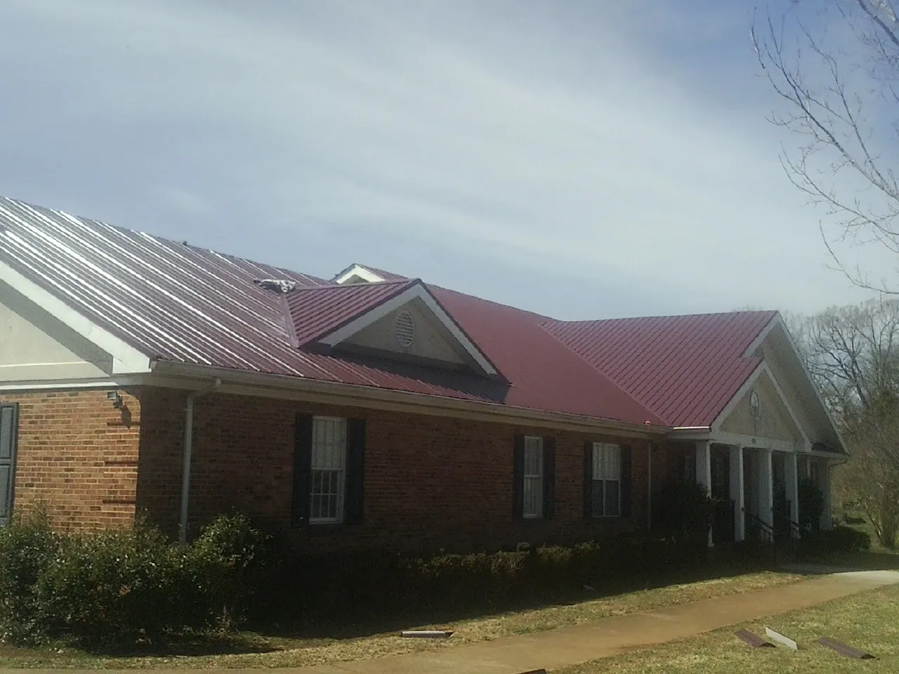 Red metal roof with gabled entries on a long brick building, from a Hail Damage Roof Repair job in Milnor