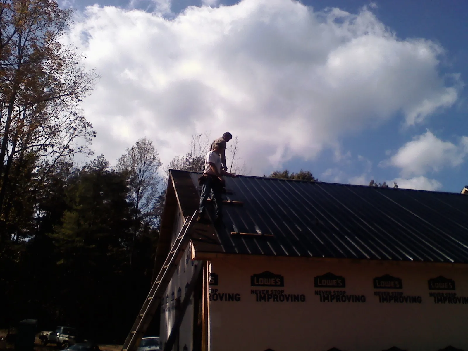 Roofer fastening dark metal panels high against a cloudy sky, from a Roof Inspection job in Milnor