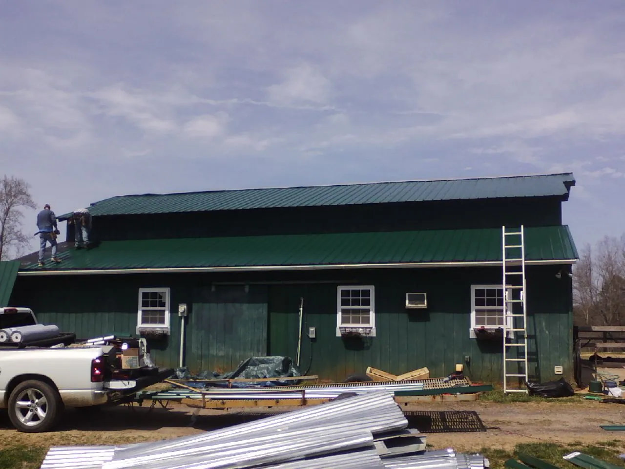 Crew installing green metal roofing on a large green barn in Milnor