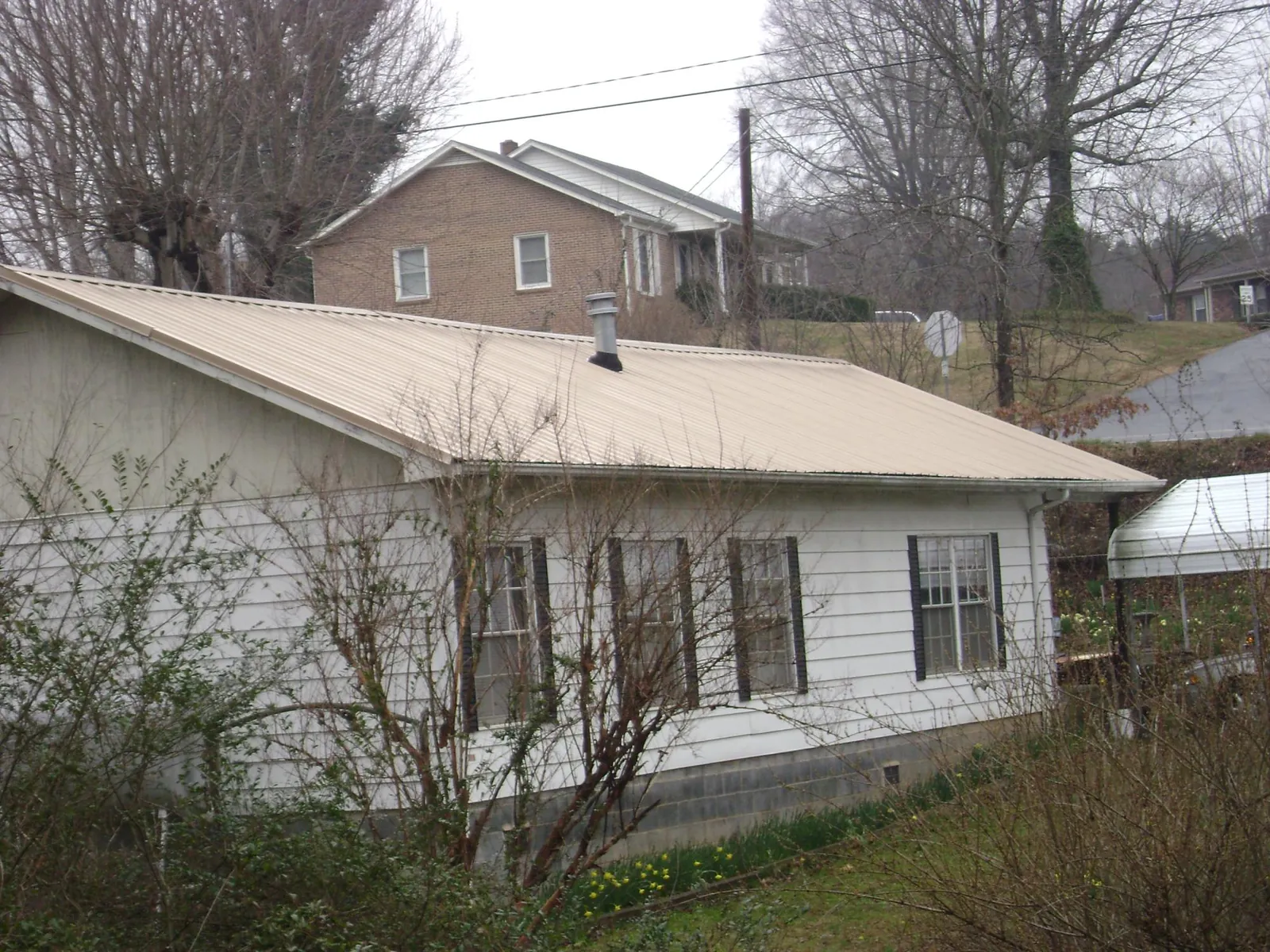 Tan metal roof on a white sided house set into a hillside — Commercial Roofing by Roofing Brothers in Milnor