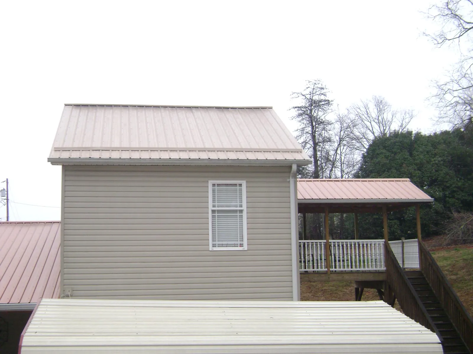 Tan metal roofs on a two story addition and attached porch, from a Roof Replacement job in Milnor